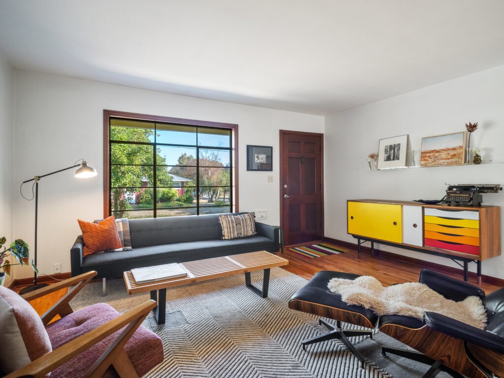 Happy young Indian couple sitting together on couch smiling while using smartphone to add chores, bills and mental load tasks in EvenUS app, warm cozy living room