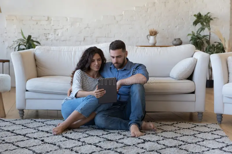 Modern couple sitting on rug using tablet together, focused and collaborative – using EvenUS app at home